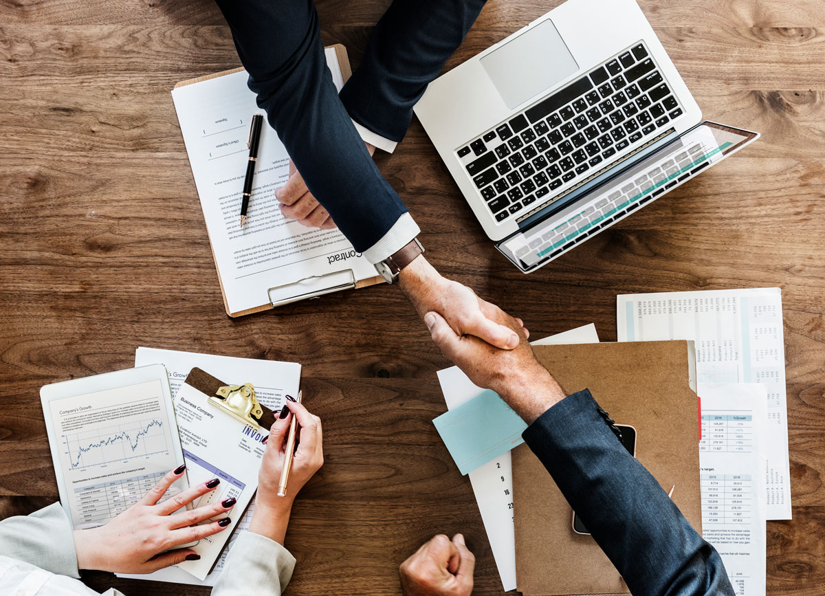 aerial photo hands shaking over desk laptop and paperwork
